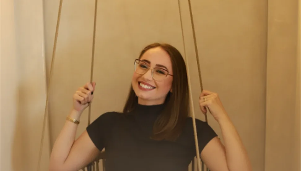 Amanda Félix sorrindo em uma cadeira suspensa no seu estúdio